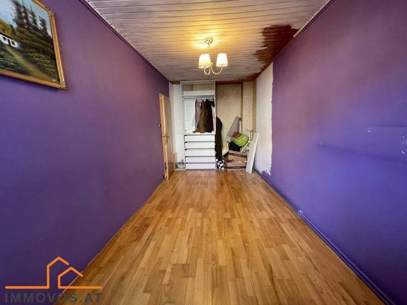Zimmer mit Holzboden, lila Wänden und einem offenen Kleiderschrankbereich.