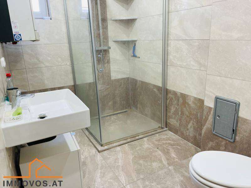 Modernes Badezimmer mit begehbarer Dusche, Waschbecken und Toilette, hell gefliest.