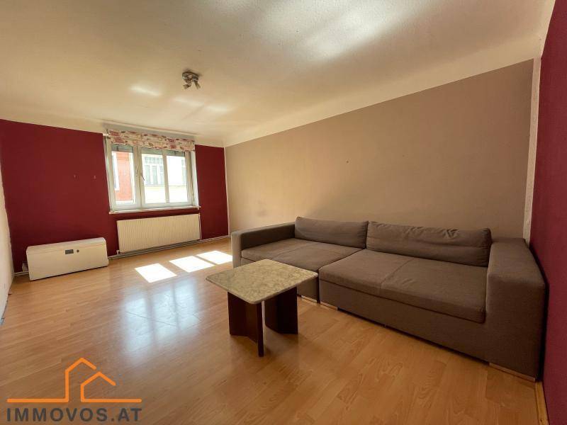 Geräumiges Wohnzimmer mit Holzboden, roter Akzentwand und einem großen Sofa.