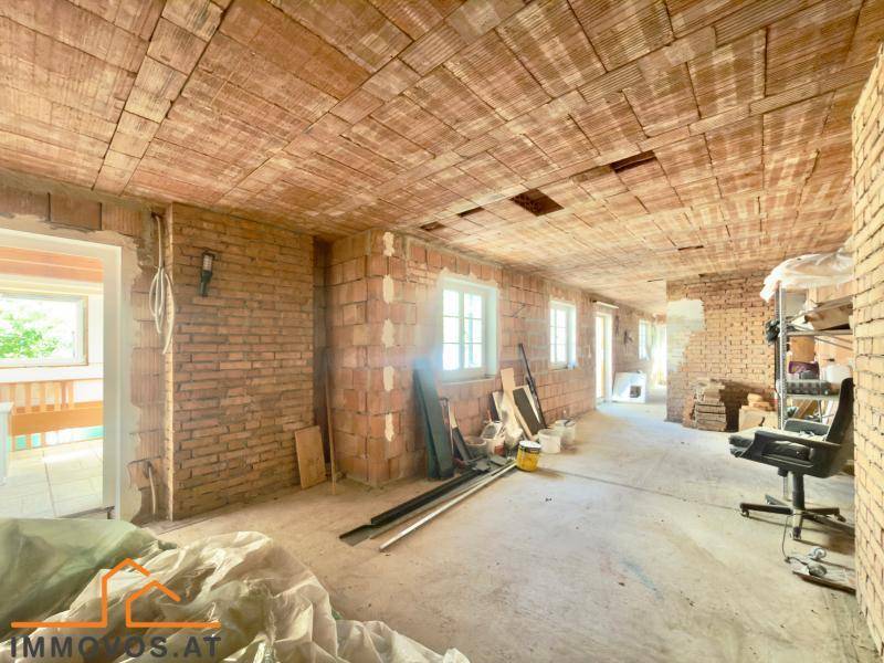 Rohbau eines Raumes mit unverputzten Ziegelwänden und Fenstern, bereit für den Ausbau.