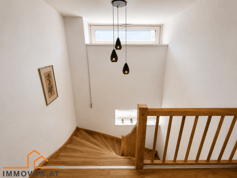 Elegante Holztreppe mit modernem Hängelicht und natürlichem Lichteinfall durch ein Fenster.