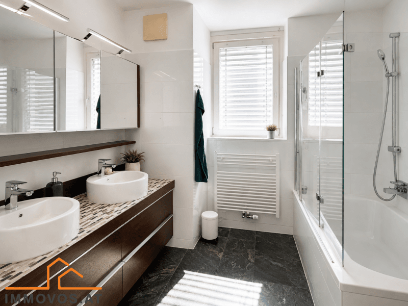 Modernes Badezimmer mit Doppelwaschbecken, Badewanne mit Dusche und Fenster für Tageslicht.