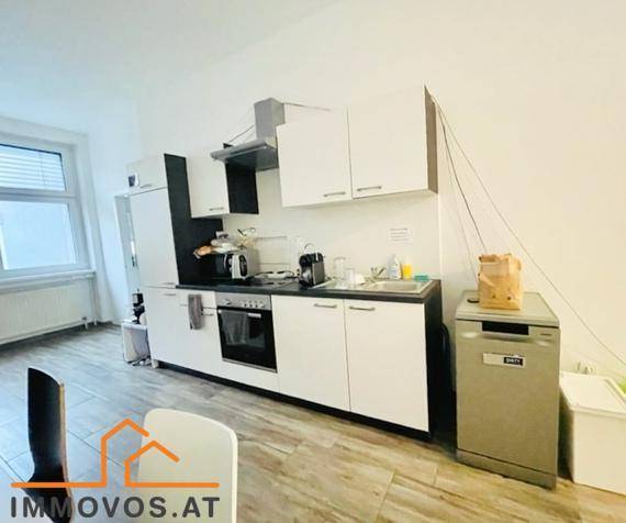 Kompakte Einbauküche mit weißen Schränken, integriertem Backofen und Geschirrspüler, sowie einem Fenster.