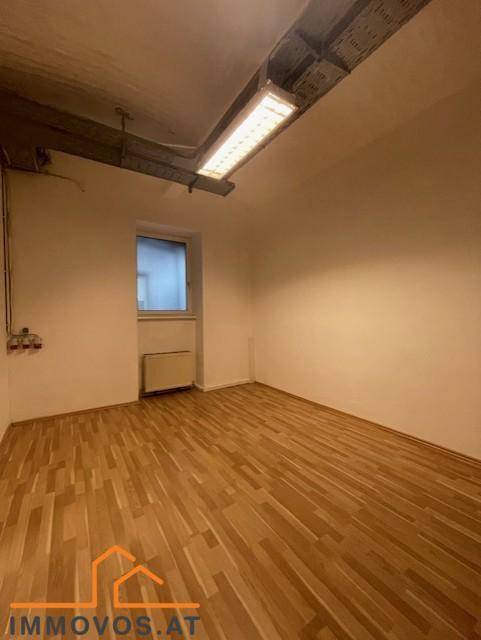 Kleinerer Raum mit Holzfußboden, einem Fenster und sichtbaren Leitungen an der Decke, gut beleuchtet.