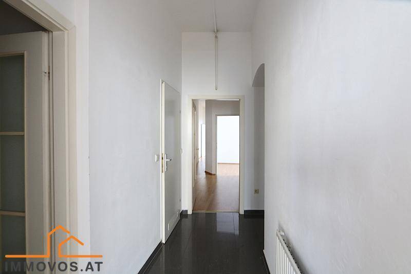 Langer Flur mit dunklem Fliesenboden und weißen Wänden, verbindet die verschiedenen Räume der Wohnung.