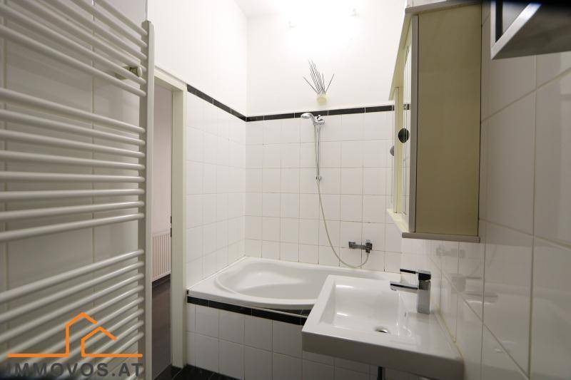 Modernes Badezimmer mit weißen Fliesen, Badewanne mit Duschfunktion und beheiztem Handtuchhalter.