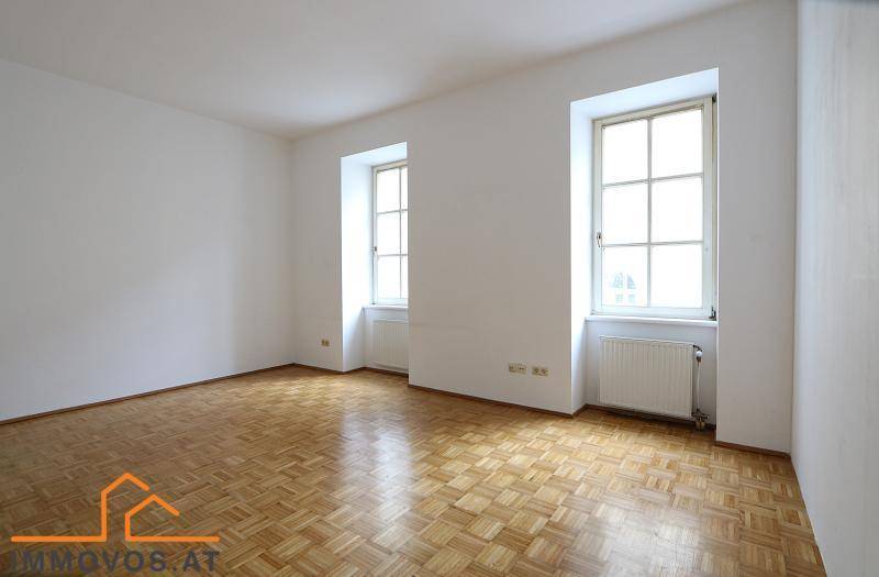Geräumiges, unmöbliertes Zimmer mit Parkettboden und zwei großen Fenstern, bietet viel Tageslicht.