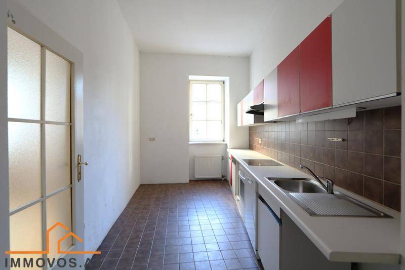 Helle Küche mit Fenster, roten Akzenten und braunem Fliesenspiegel, bietet ausreichend Arbeitsfläche.