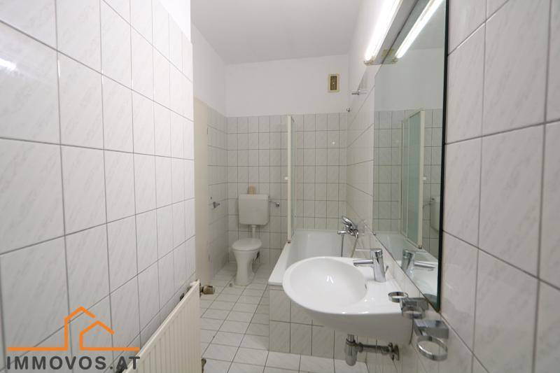 Gefliestes Badezimmer mit Badewanne, WC, Waschbecken und großem Spiegel, in gutem Zustand.