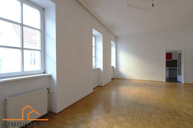Lichtdurchfluteter Raum mit Parkettboden und Zugang zu einer Küche, ideal für einen offenen Wohnbereich.
