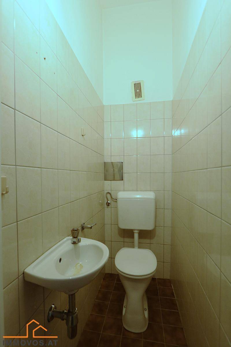 Separates WC mit beigen Wandfliesen, Toilette und kleinem Eckwaschbecken.
