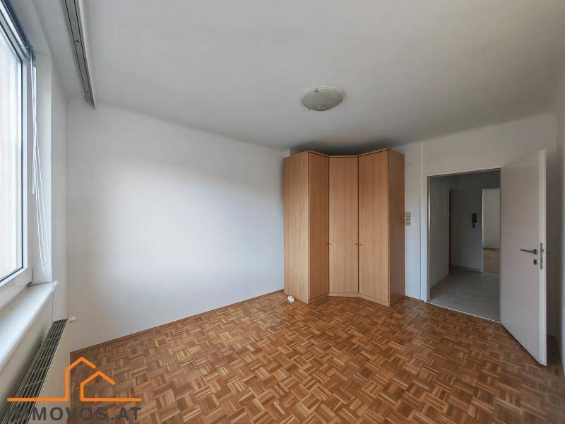 Schlafzimmer mit Parkettboden, großem Fenster und eingebautem Eckschrank.