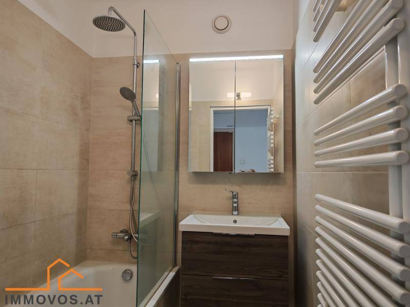 Helles Badezimmer mit Badewanne, Duschkopf und beheiztem Handtuchhalter.