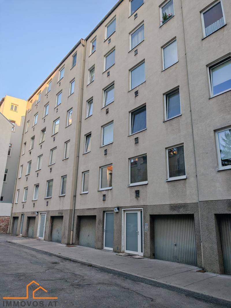 Rückseite eines Wohngebäudes mit mehreren Garagen und Fenstern.