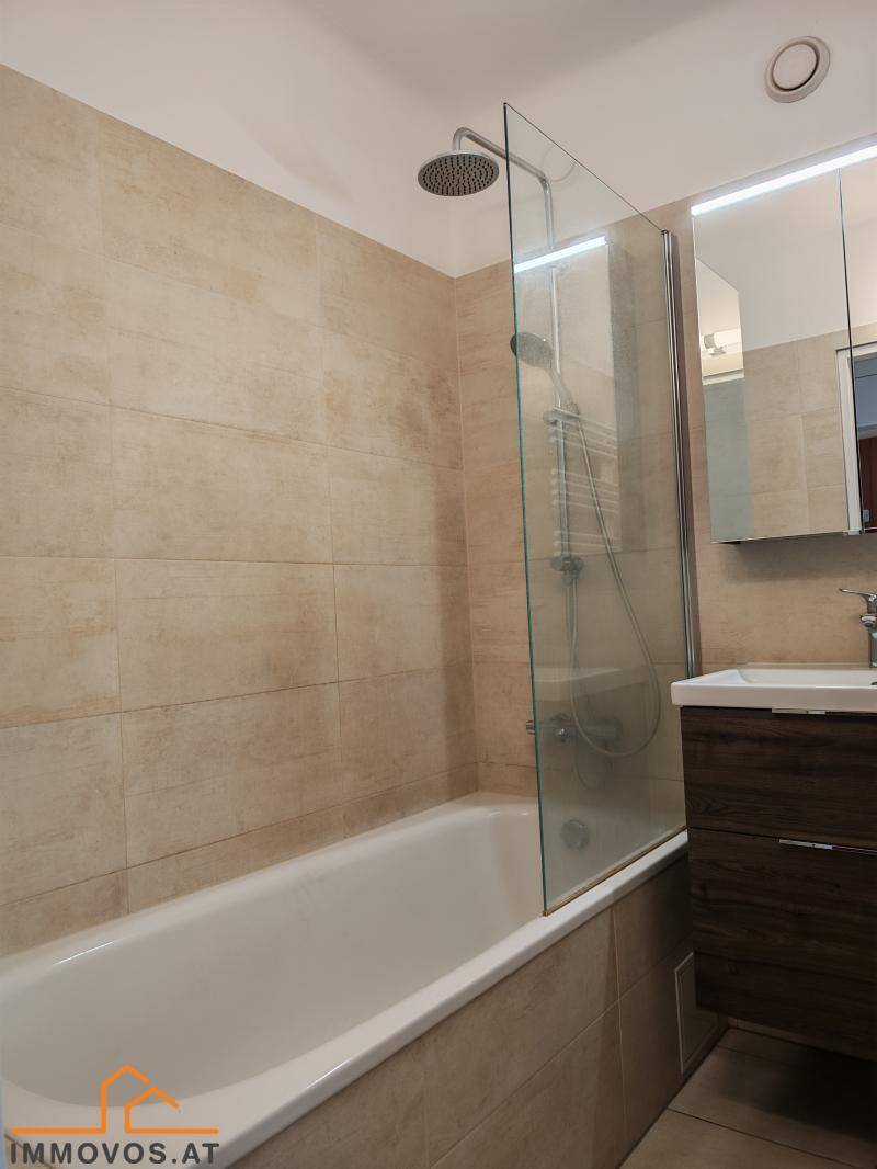 Modernes Badezimmer mit Badewanne, Duschvorrichtung und beigefarbenen Fliesen.