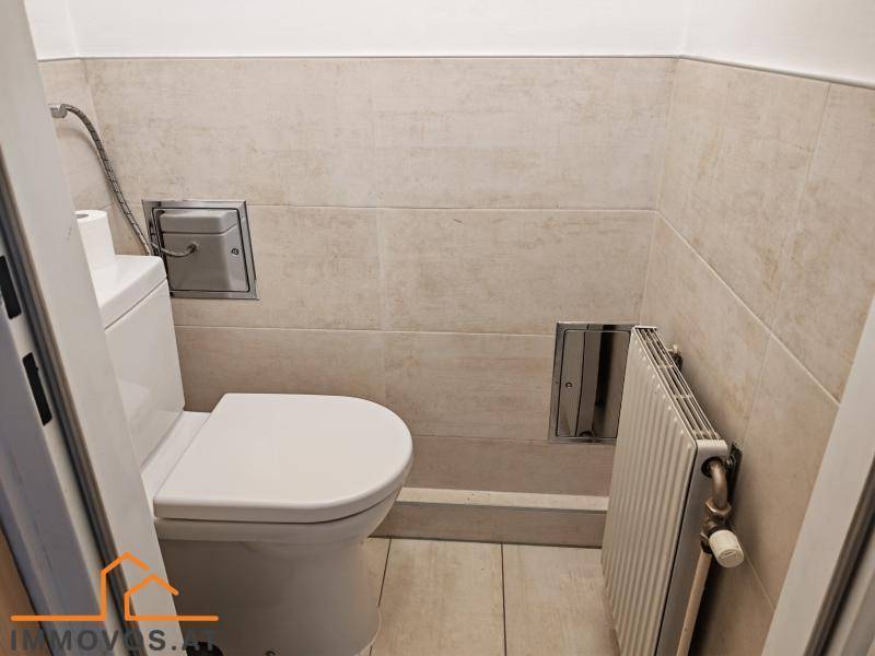 Kleines WC mit beigefarbenen Fliesen, Heizkörper und einfacher Toilette.