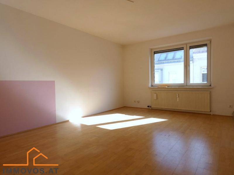 Leeres Wohnzimmer mit Holzboden, weiß gestrichenen Wänden und viel natürlichem Lichteinfall durch das Fenster.