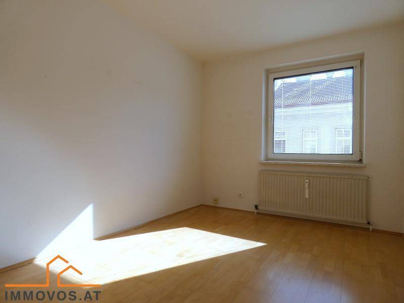 Leeres Schlafzimmer mit Holzboden, weiß gestrichenen Wänden und natürlichem Lichteinfall durch das Fenster.