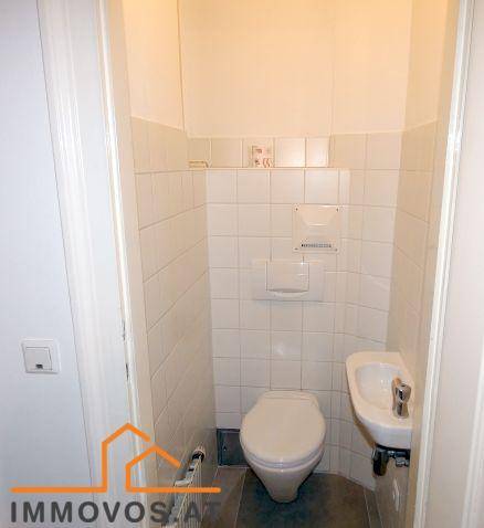 Kompaktes Gäste-WC mit weißen Fliesen, wandhängendem WC und einem kleinen Handwaschbecken.