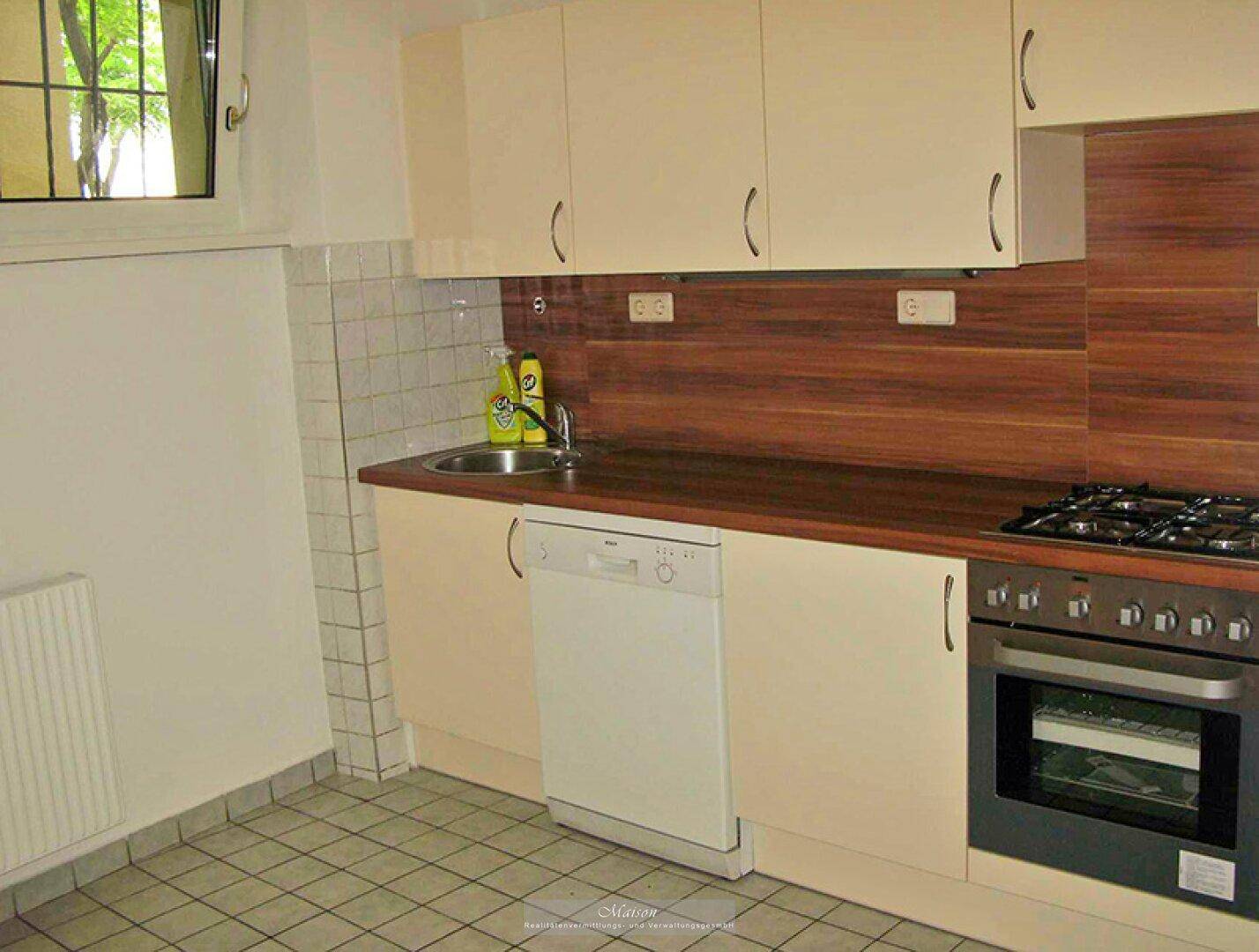 Funktionale Küche mit beigen Schränken, Holzoptik-Arbeitsplatte und integriertem Geschirrspüler.