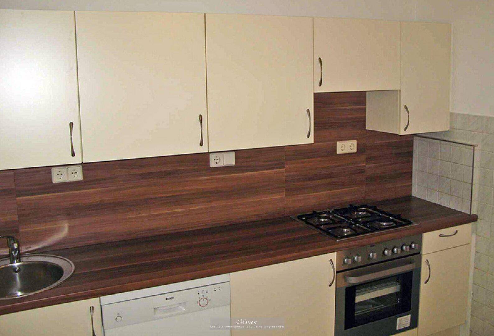 Einbauküche mit hellen Fronten, Holzdekor-Arbeitsplatte und Gasherd mit Backofen.
