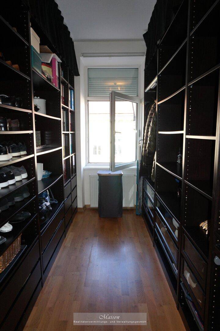 Geräumiger begehbarer Kleiderschrank mit dunklen Regalen und einem Fenster für natürliche Belüftung.