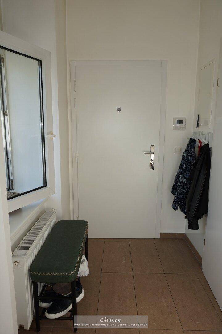 Heller Eingangsbereich mit Fliesenboden, Garderobe und einer modernen Eingangstür.