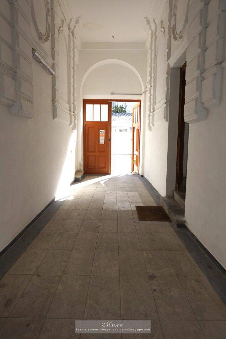 Heller, gefliester Eingangsbereich eines Mehrfamilienhauses mit hohen Decken und Holztüren.