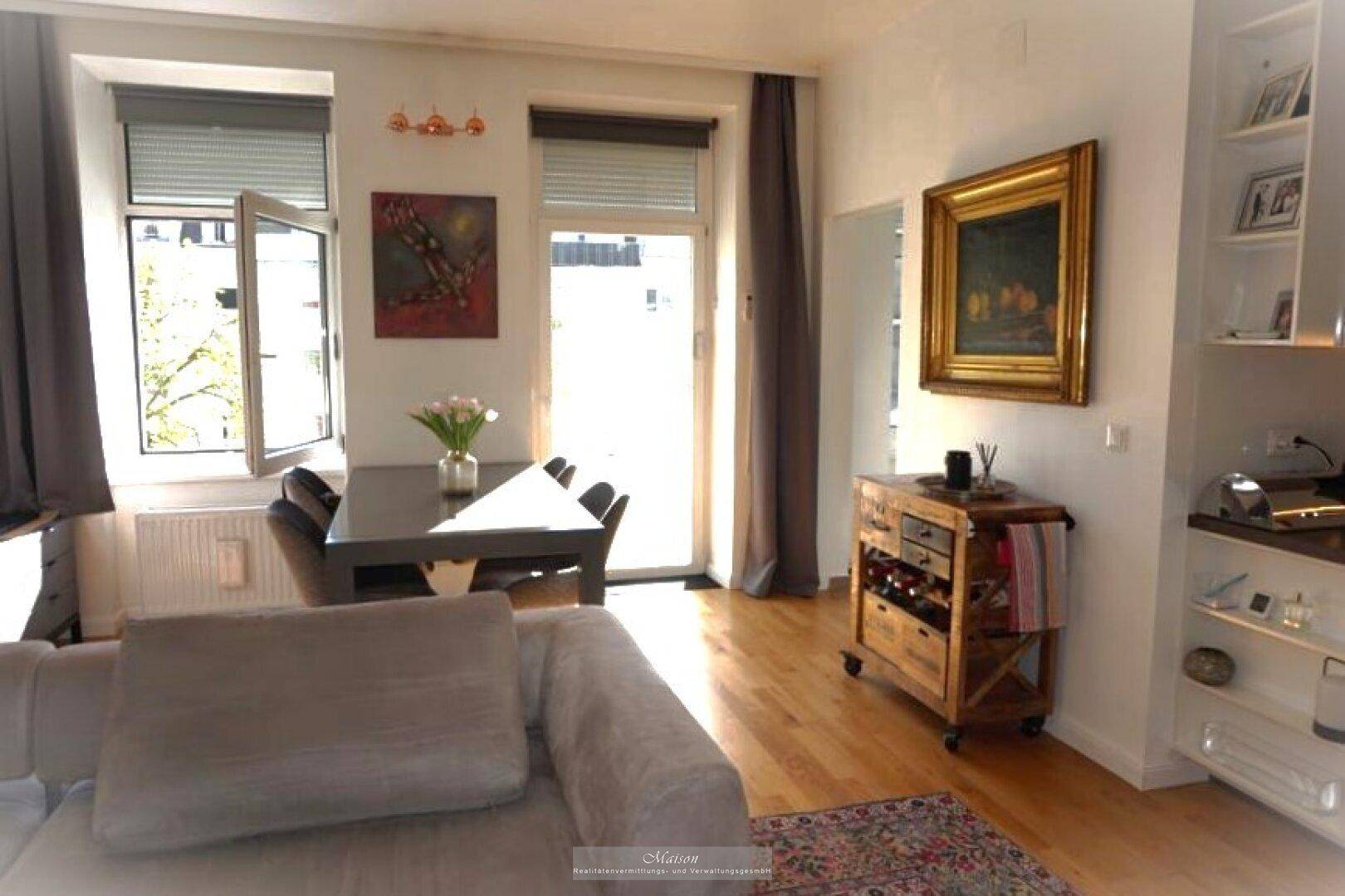 Lichtdurchfluteter Wohnbereich mit Esstisch, Holzboden und Zugang zu einem Balkon.