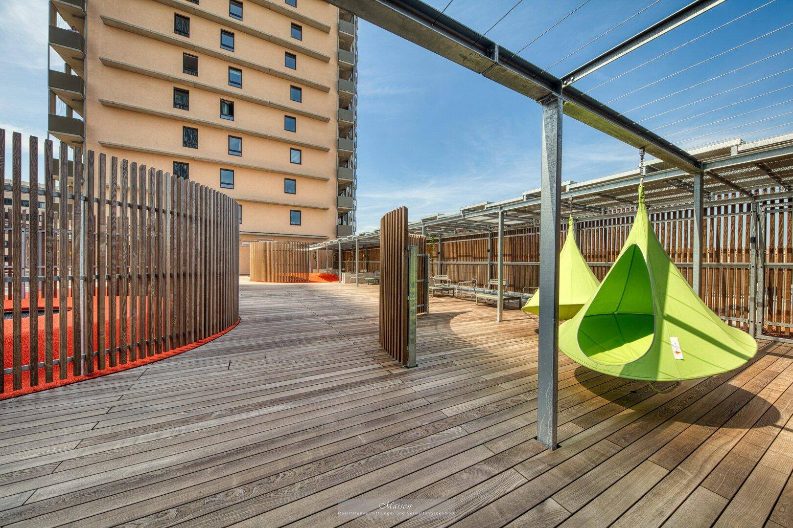 Große Dachterrasse mit Holzdeck, Hängesesseln und Blick auf die umliegenden Gebäude.