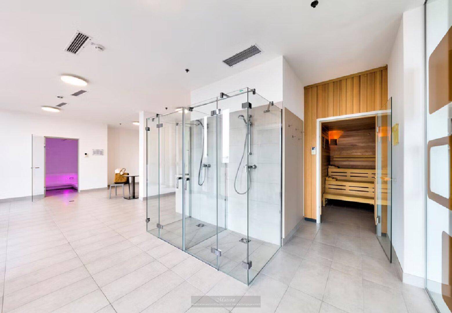 Geräumiger Wellnessbereich mit mehreren Duschkabinen und dem Eingang zur holzvertäfelten Sauna.