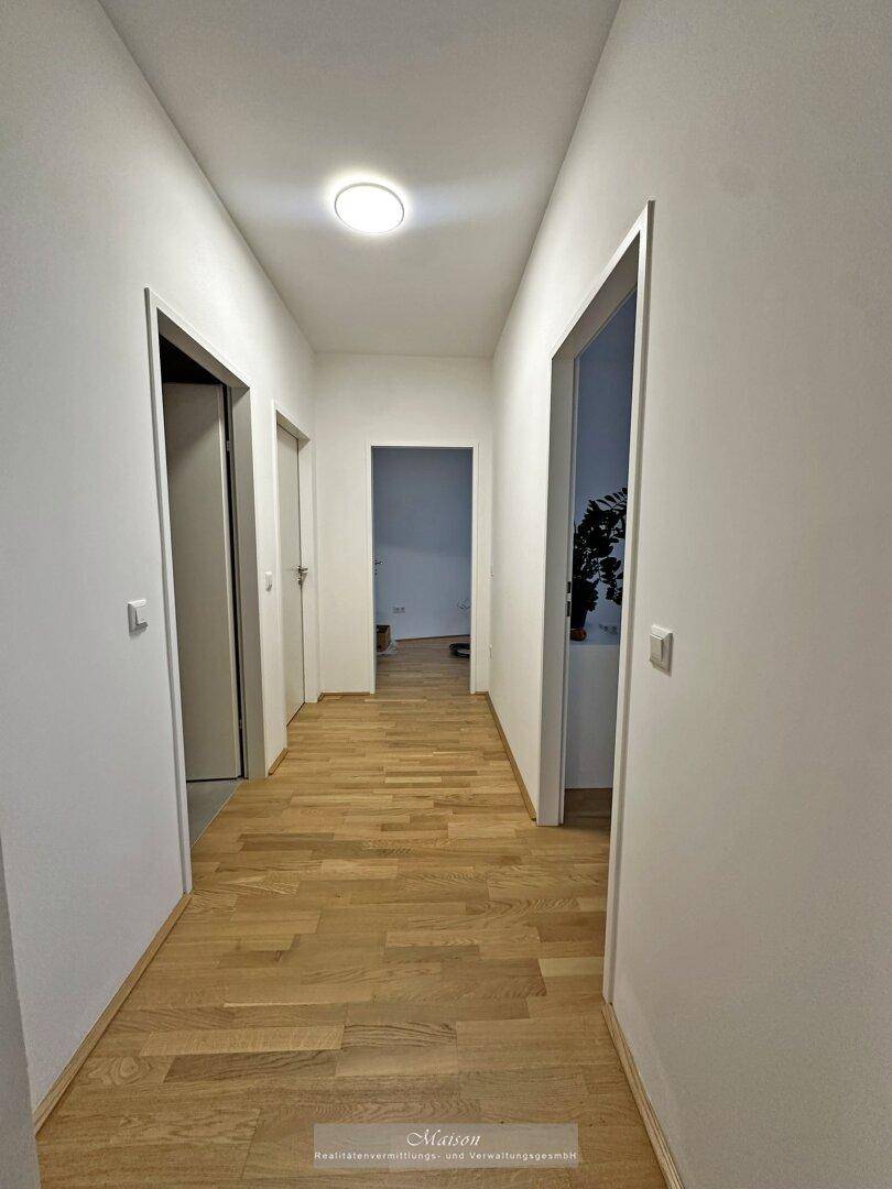 Heller Flur mit hellem Holzparkett und weißen Wänden, der zu weiteren Räumen führt.
