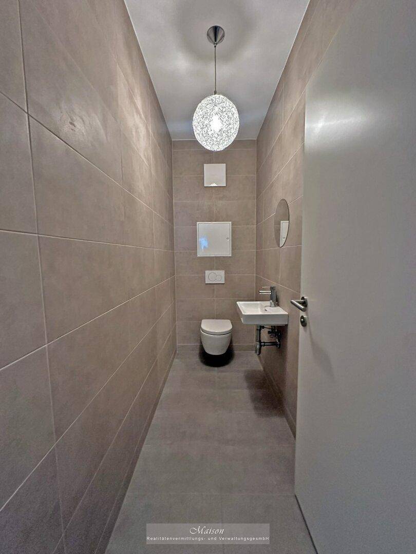Kompaktes Gäste-WC mit Wand-WC, kleinem Waschbecken und moderner Deckenleuchte.