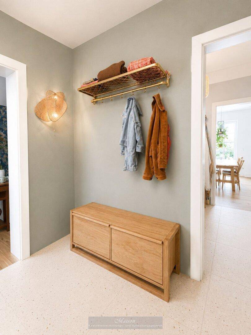 Flur mit heller Wandfarbe, Holzbank und goldener Garderobenstange.
