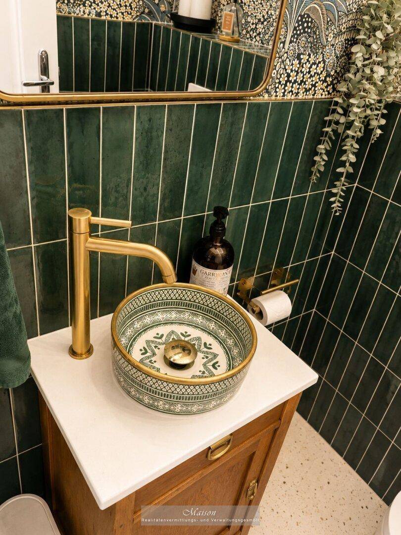 Stilvolles Gäste-WC mit grünen Fliesen, goldenem Wasserhahn und gemusterter Waschschale.