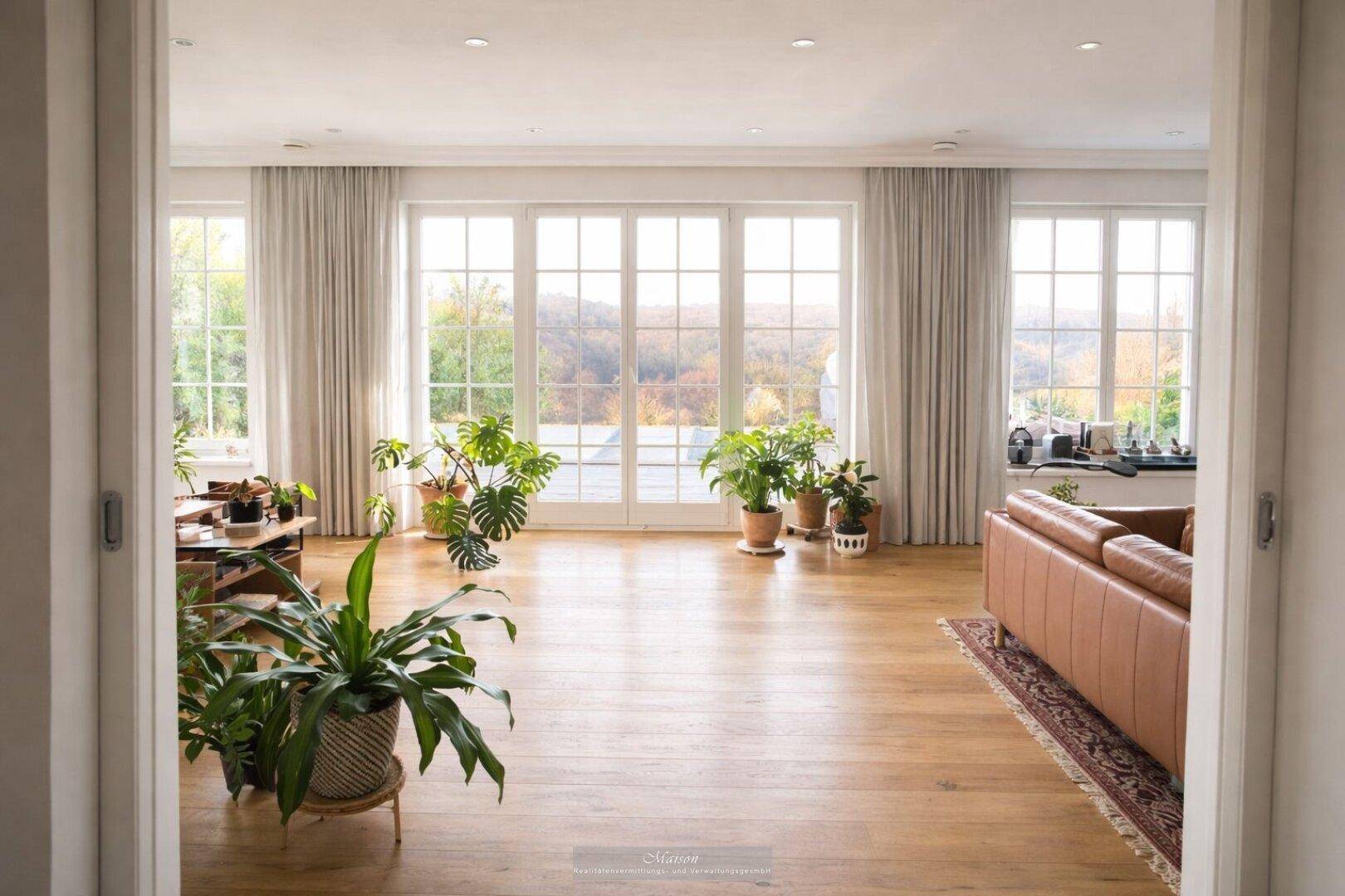 Großes Wohnzimmer mit vielen Pflanzen, Holzboden und weitem Blick ins Grüne.