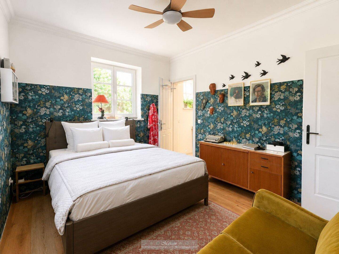 Schlafzimmer mit floraler Tapete, Holzboden und Deckenventilator.