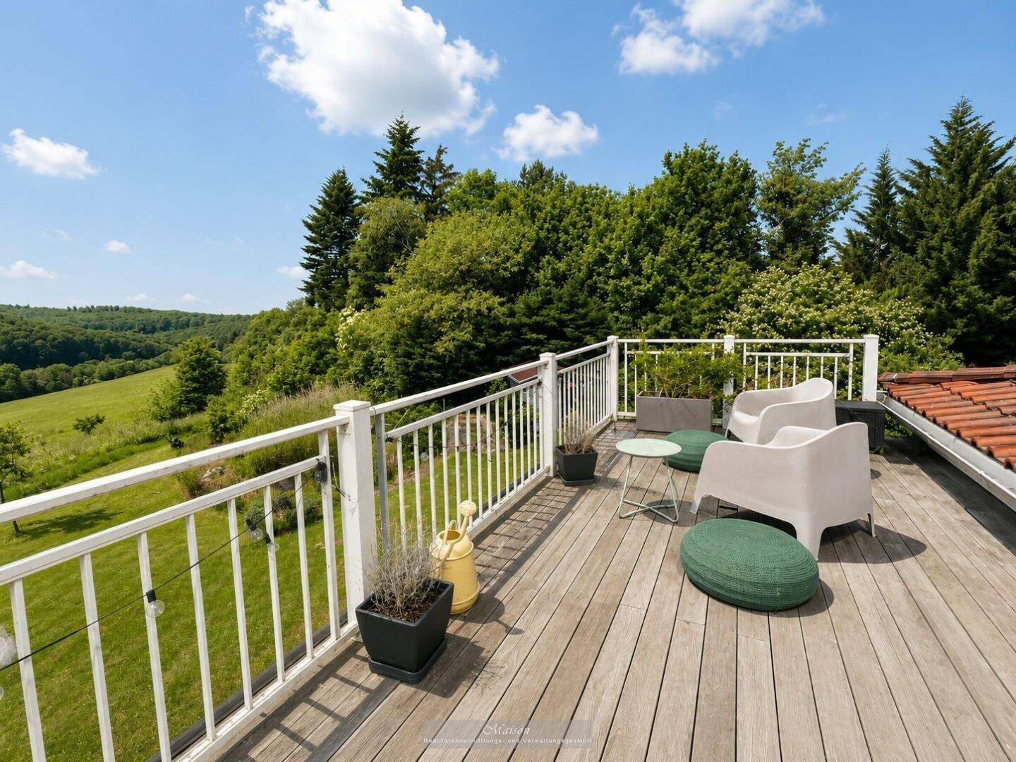 Große Holzterrasse mit Sitzgelegenheiten und weitem Blick ins Grüne.
