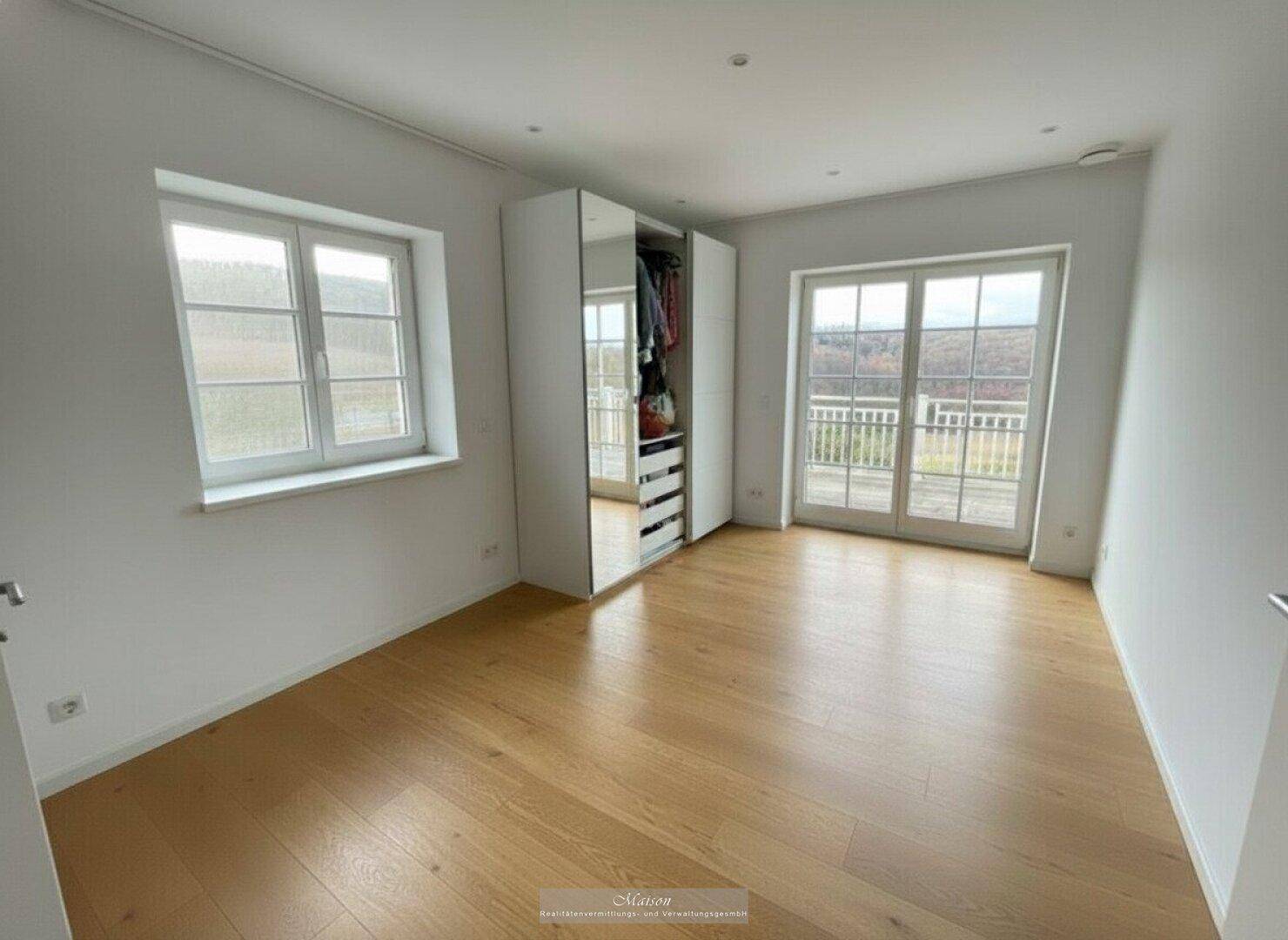 Helles Schlafzimmer mit Parkettboden, Spiegelschrank und Zugang zum Balkon.