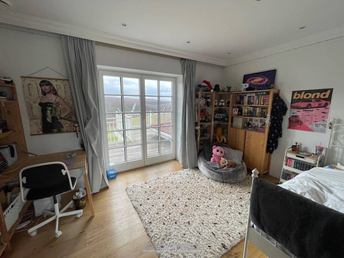 Jugendzimmer mit Schreibtisch, Bücherregal und Zugang zum Balkon.