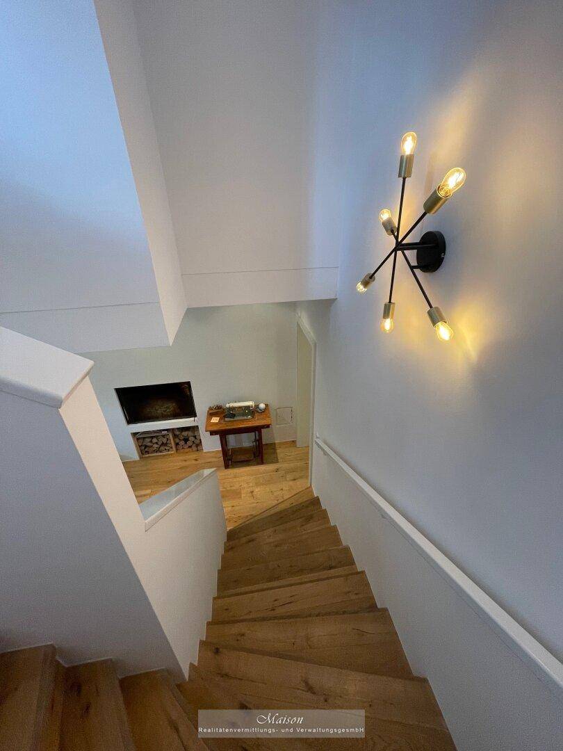 Treppenhaus mit Holzstufen und moderner Wandbeleuchtung.