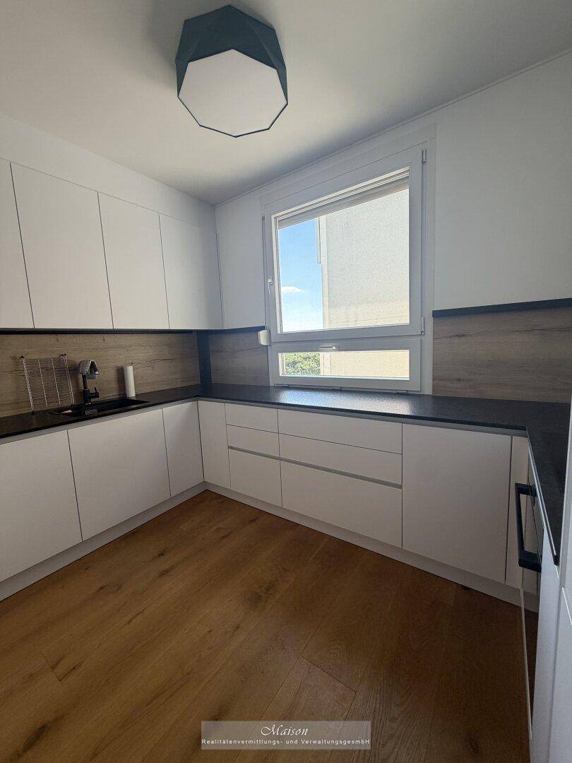Moderne Küche mit weißen Schränken, dunkler Arbeitsplatte und einem Fenster für natürliches Licht.