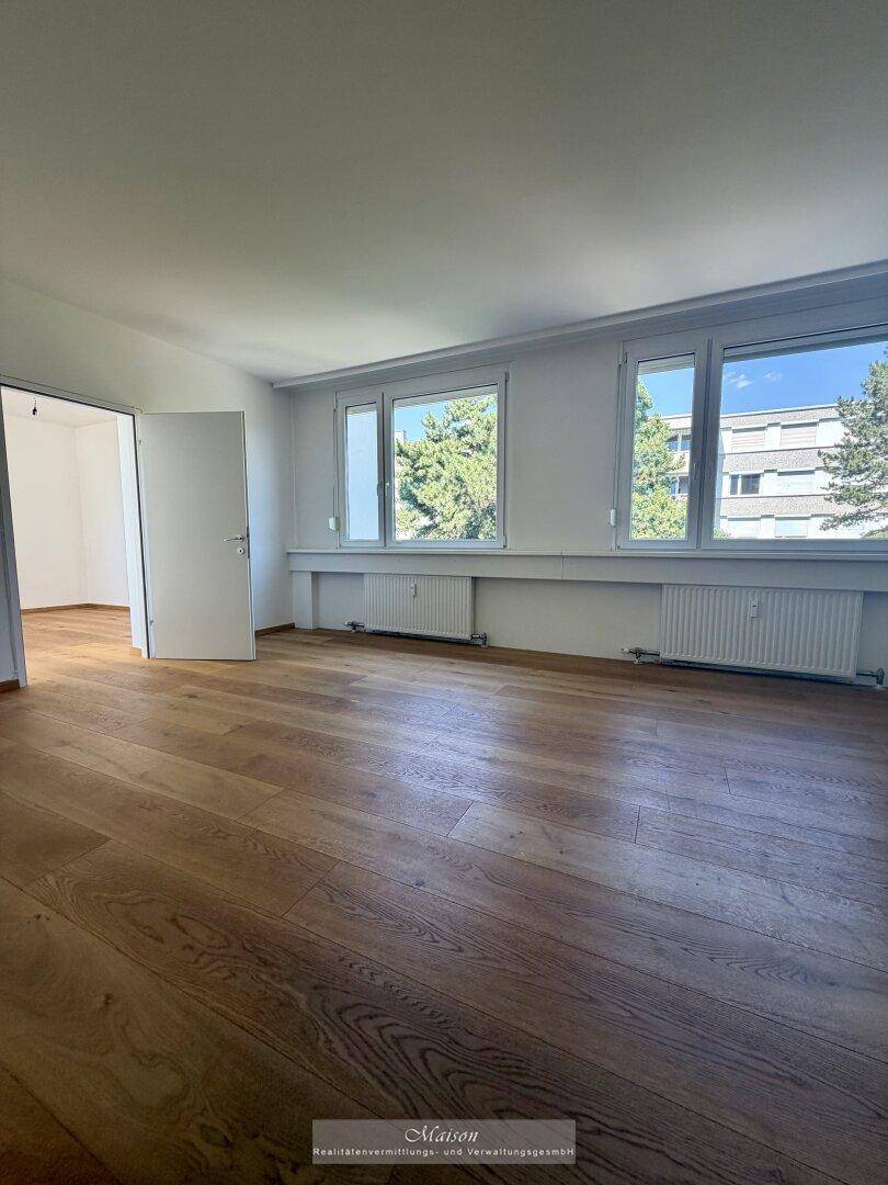 Großes, helles Wohnzimmer mit Holzparkettboden und mehreren Fenstern für reichlich Tageslicht.