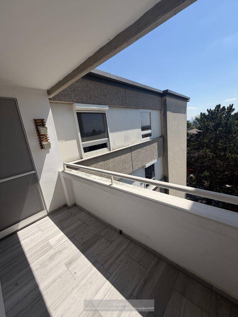Sonniger Balkon mit Fliesenboden und Blick auf die umliegenden Gebäude und den blauen Himmel.