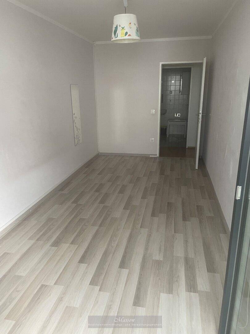 Helles Zimmer mit Laminatboden und Zugang zu einem weiteren Raum.