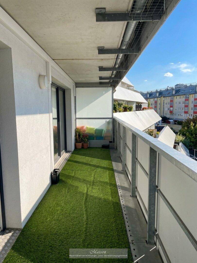 Schmaler Balkon mit Kunstrasen und Blick auf die umliegenden Gebäude.