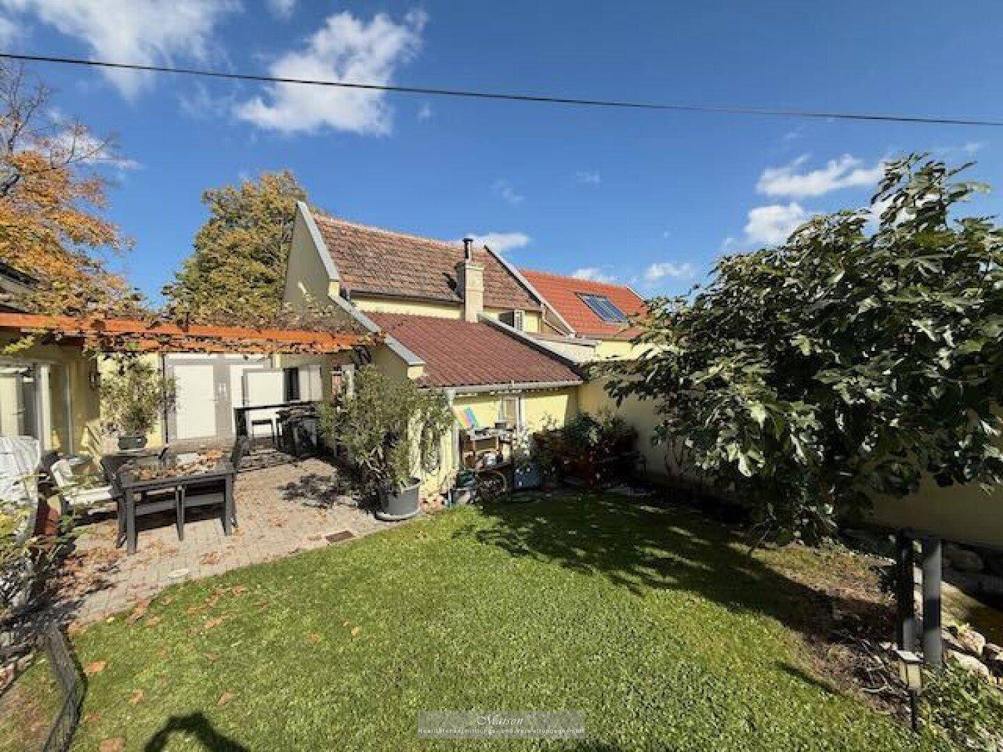 Weitläufiger Gartenbereich mit Rasen, Bäumen und einer gemütlichen Terrasse am Haus.