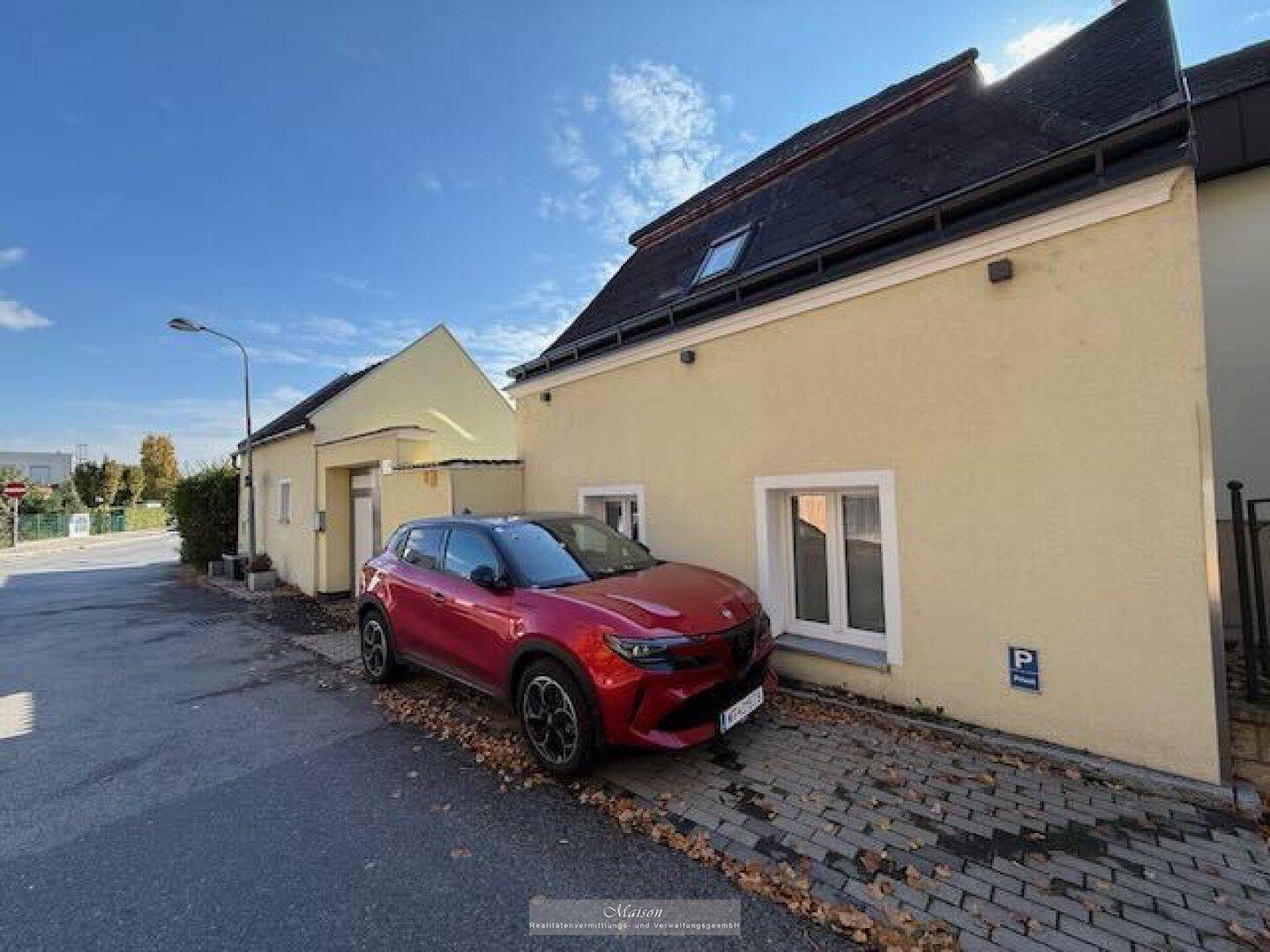 Fassade des Hauses von der Straße aus mit einem geparkten Auto und kleiner Einfahrt.