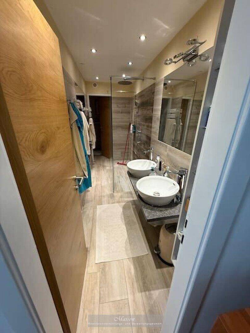 Modernes Badezimmer mit Doppelwaschbecken, begehbarer Dusche und Holzoptik-Fliesen.