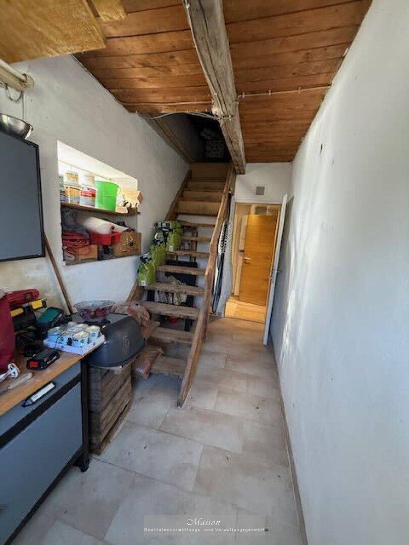 Funktionaler Bereich mit Holztreppe, Stauraum und sichtbaren Holzbalken an der Decke.